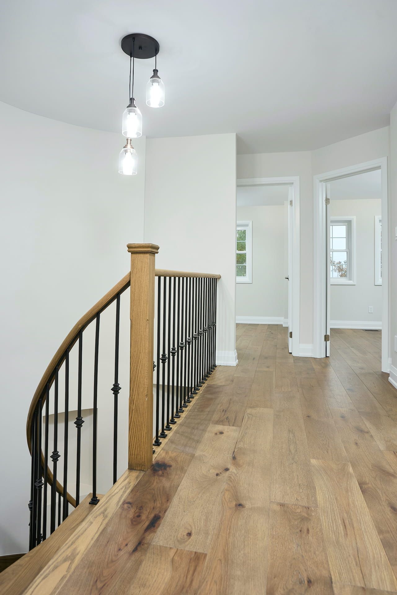 Hallway with wooden floor, stairs with black railing, and pendant lights.