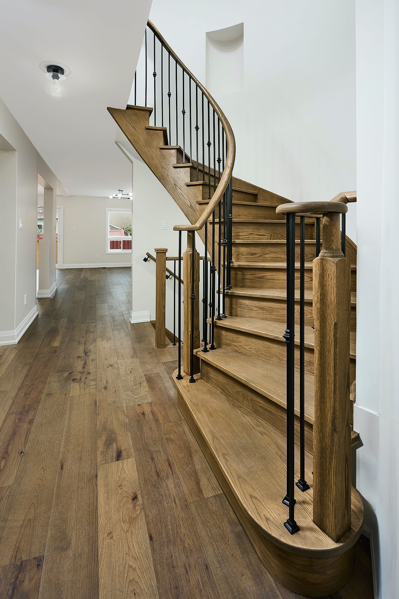 Wooden curved staircase with black railings, next to a hardwood floor hallway.