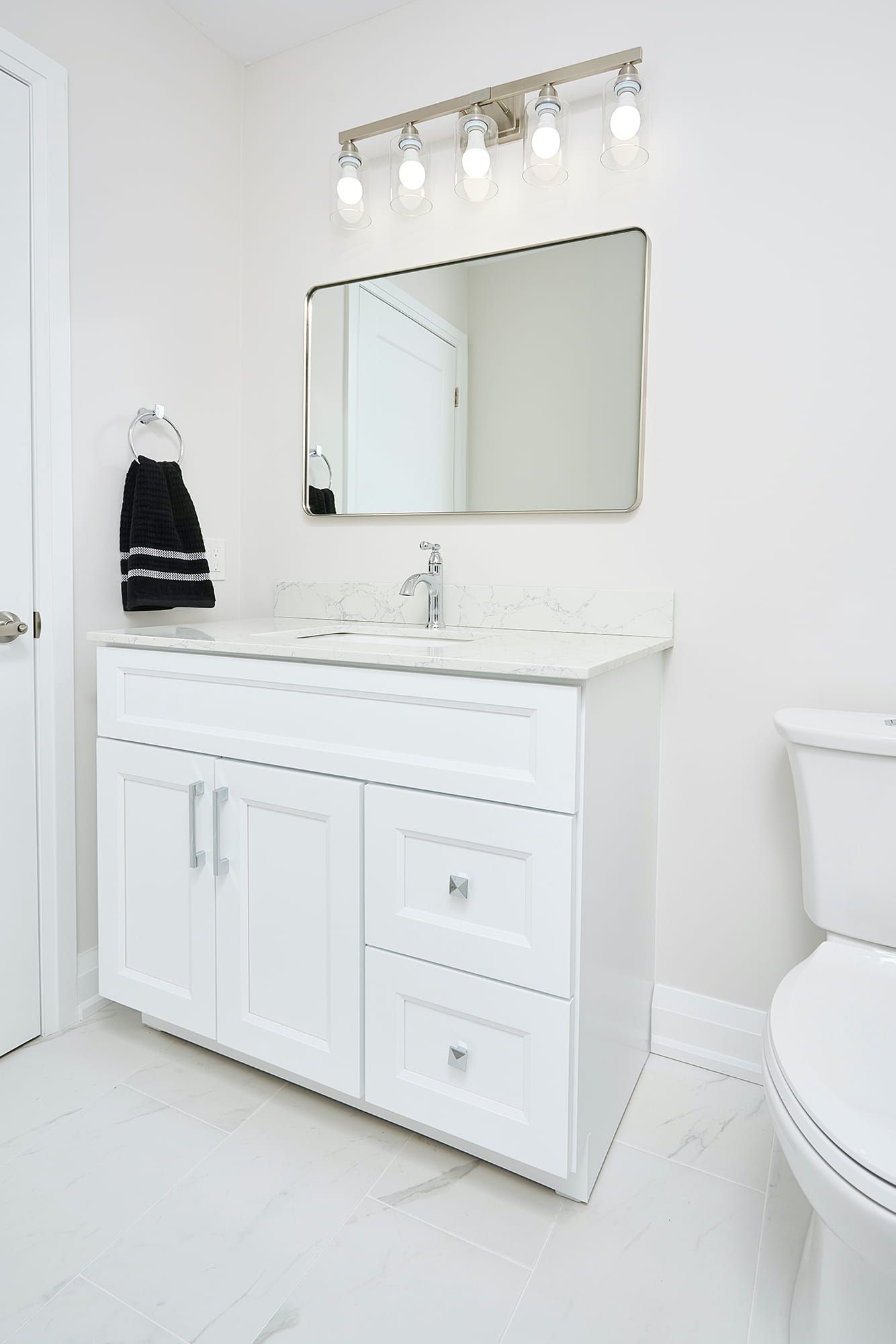 White bathroom with vanity, mirror, toilet, and towel.