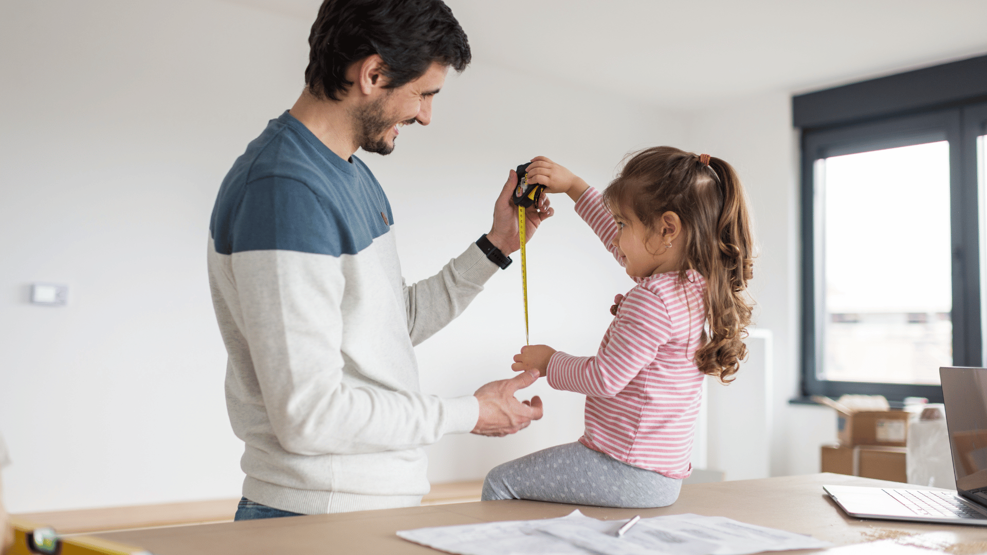 Man showing child a measuring tape on a table; they are smiling during full home renovation.