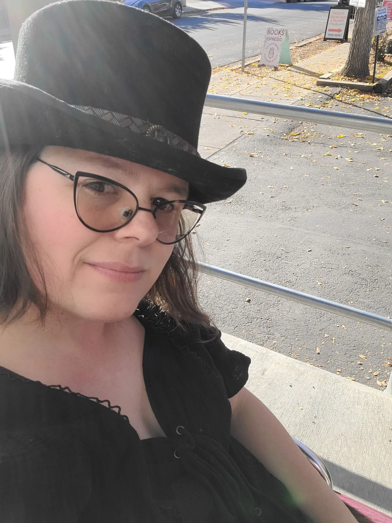 Woman wearing glasses and a black top hat, sitting outside.