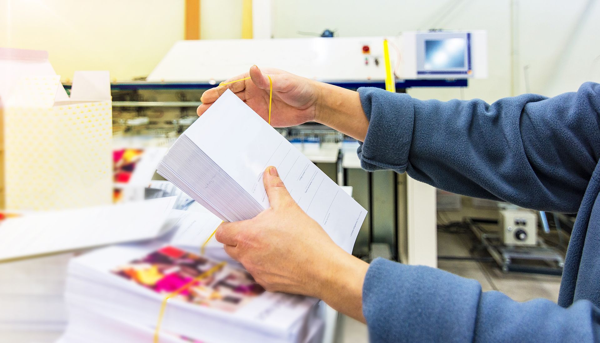 Person holding printed papers, examining them in a print shop.