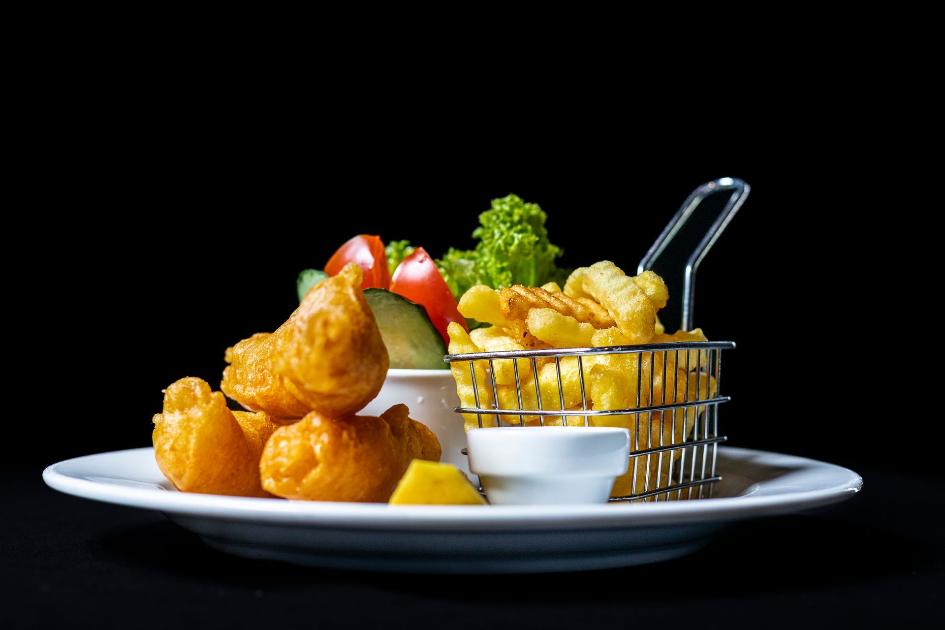 Fish and chips with salad and dipping sauce on a white plate.