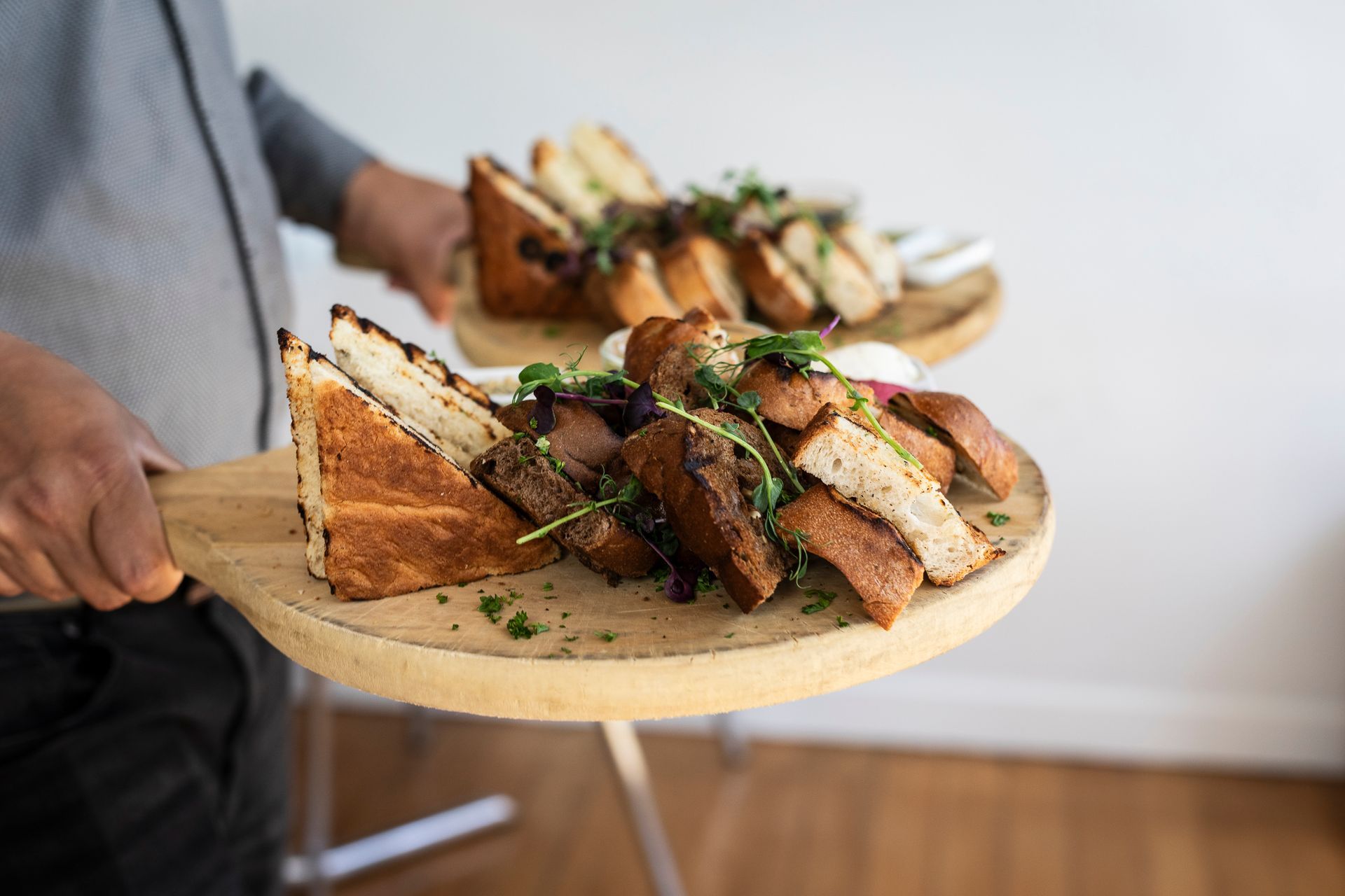Person holding wooden platters of toasted bread and garnishes.