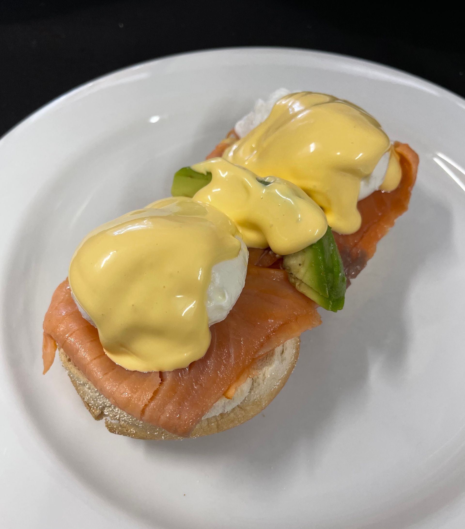 Eggs Benedict with smoked salmon and avocado on a toasted bread slice, topped with hollandaise sauce.