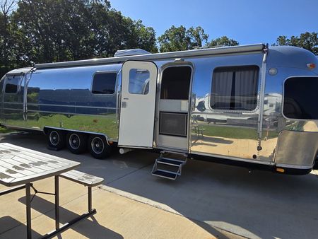 A silver airstream trailer is driving down a dirt road.