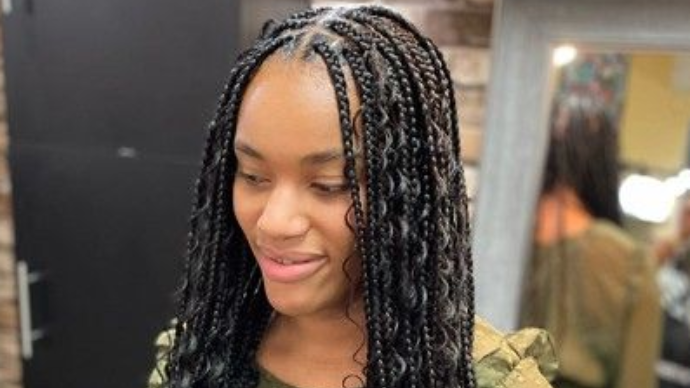 Woman with long black braids, some wavy, smiling, indoors.
