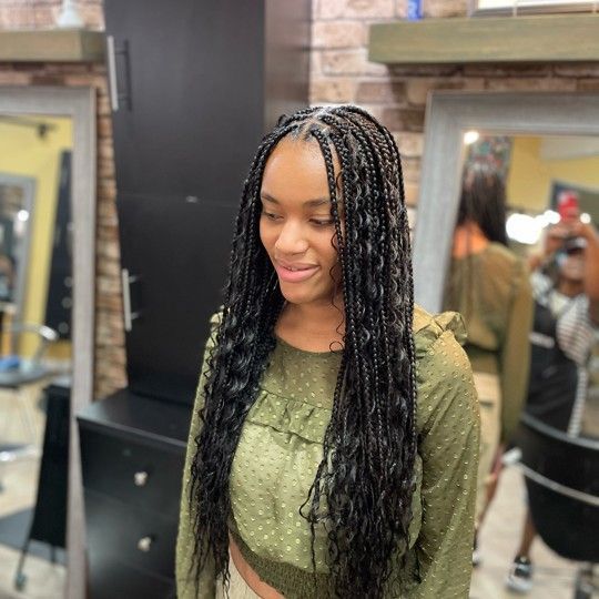 Woman with long, wavy, black braids wearing a green shirt in a hair salon.