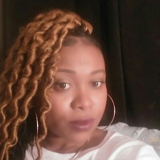 Woman with blonde faux locs and large hoop earrings.