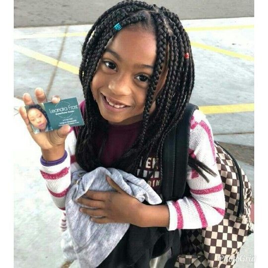 Girl with braids smiles, holding a business card, wearing a striped shirt and backpack.