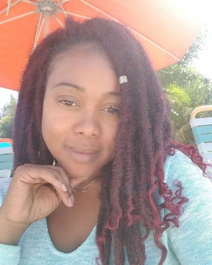 Woman with burgundy dreadlocks, looking at the camera, outdoors under an orange parasol.