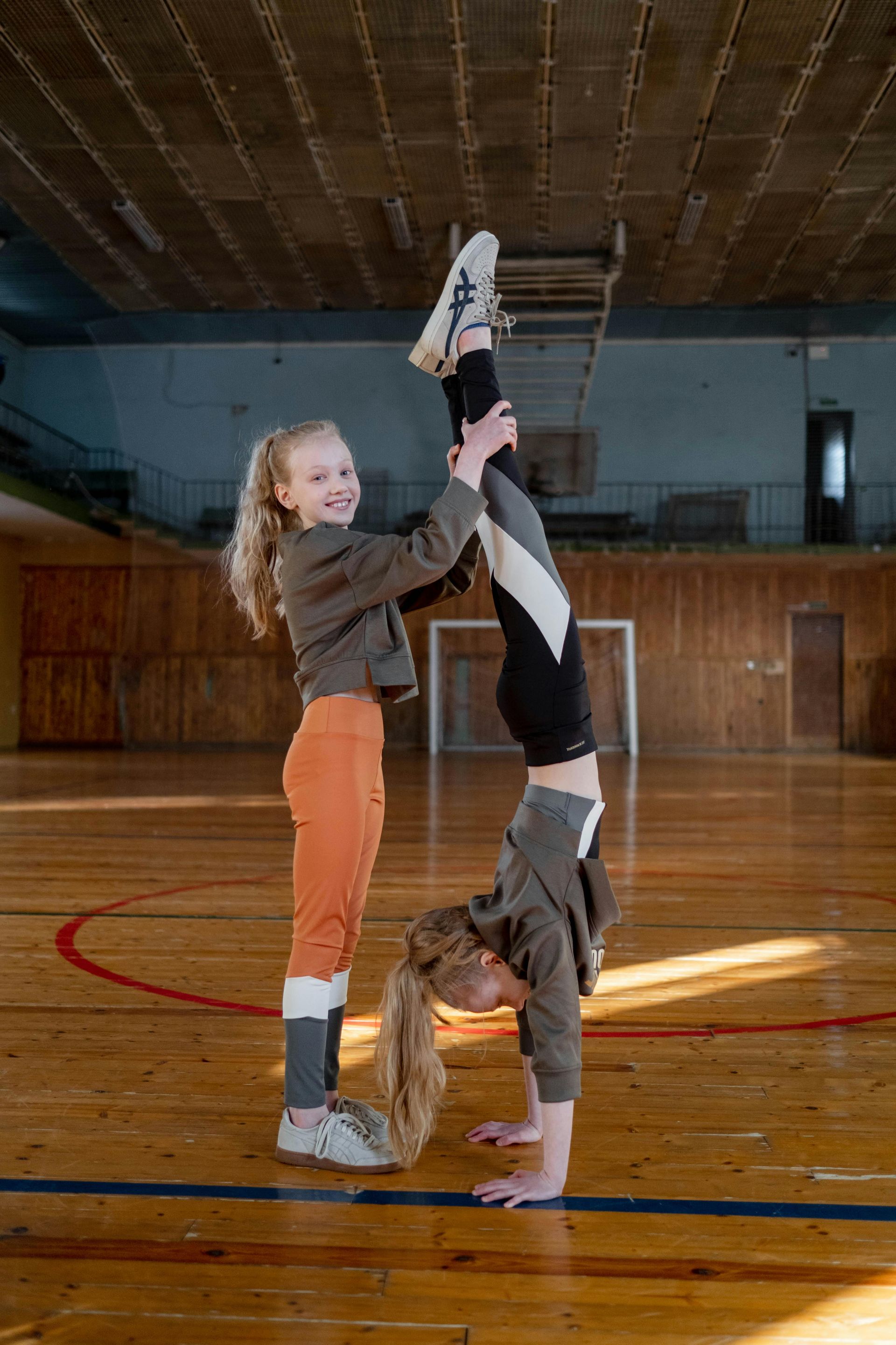 Two little girls are doing a handstand in a gym.