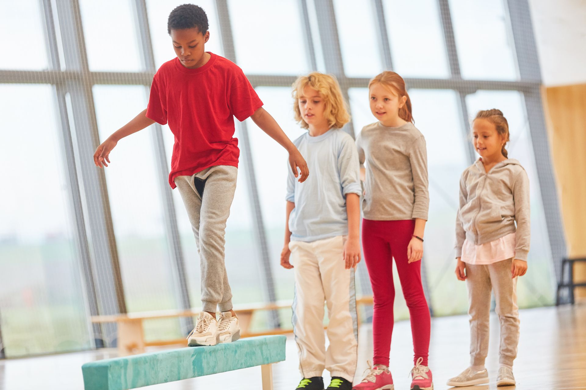 A group of children are standing on a balance beam in a gym.