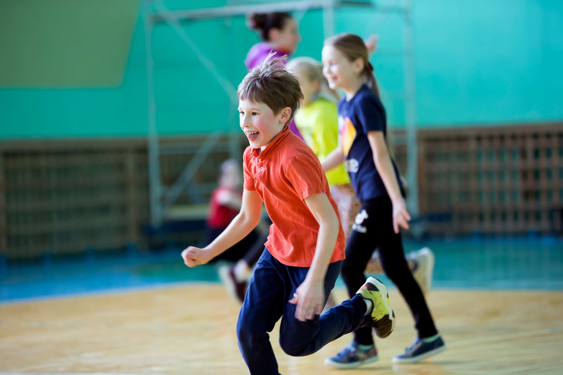 A group of children are running on a wooden floor in a gym.