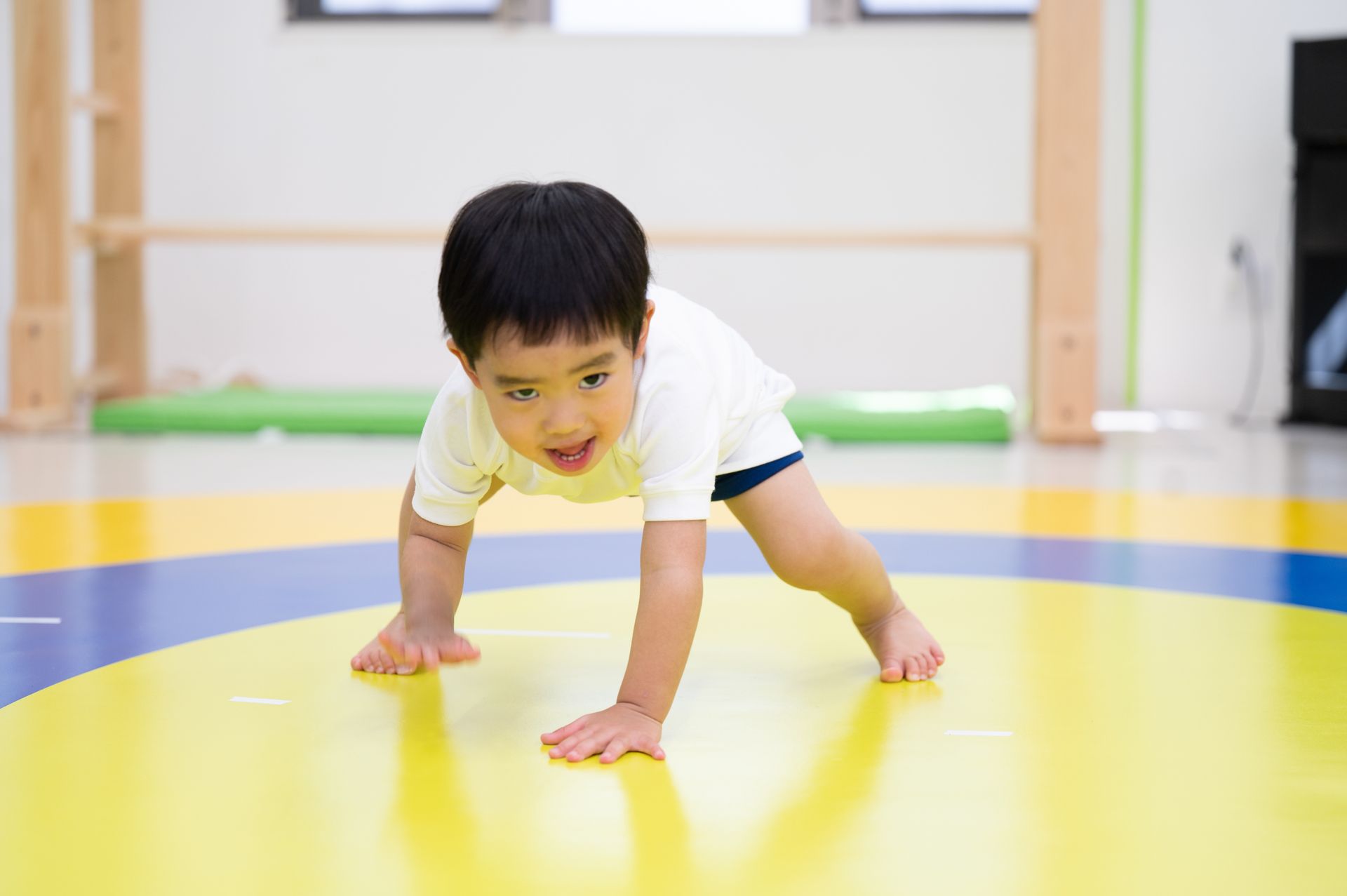 A young boy is crawling on a yellow mat in a gym.