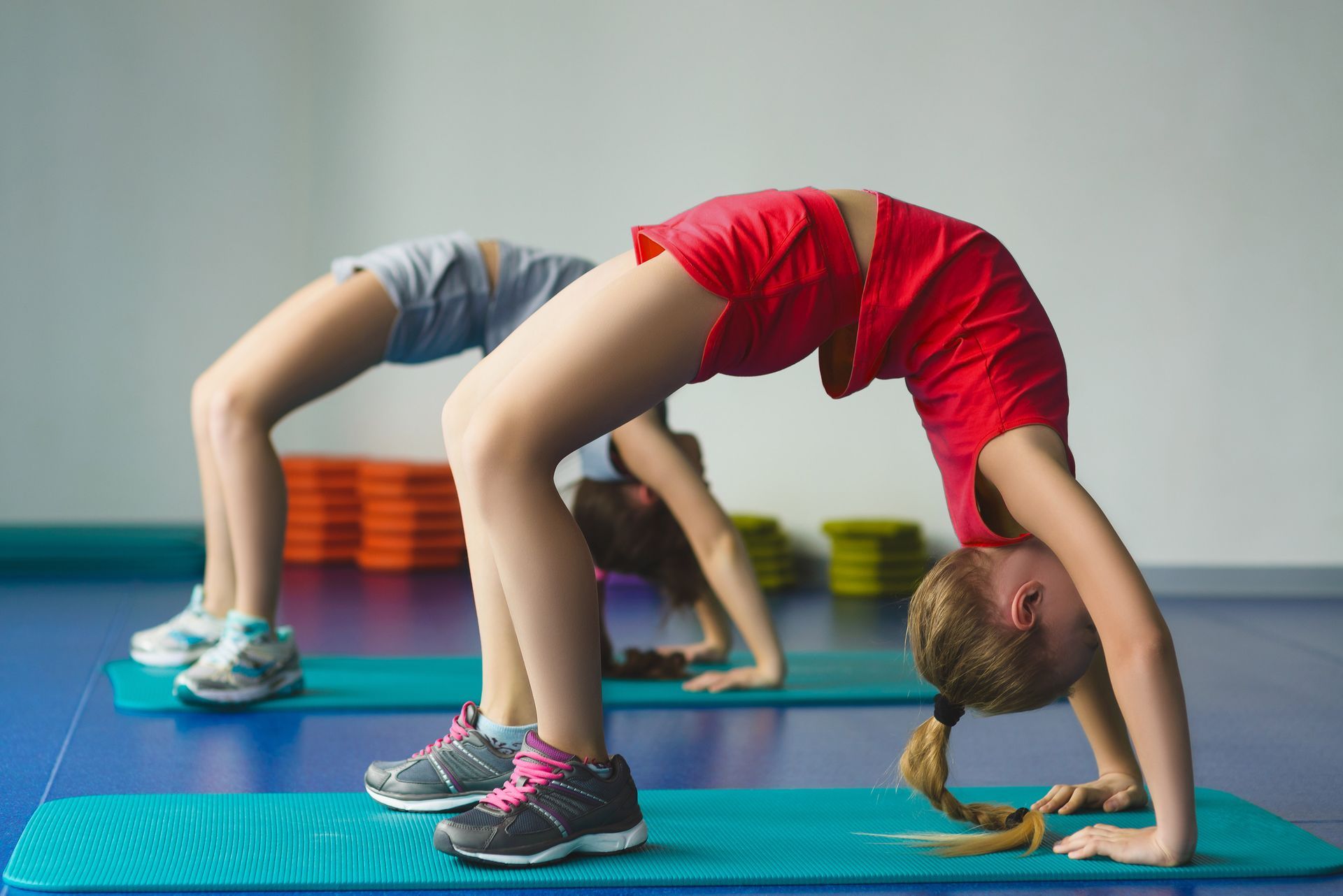 Two young girls are doing exercises on yoga mats in a gym.