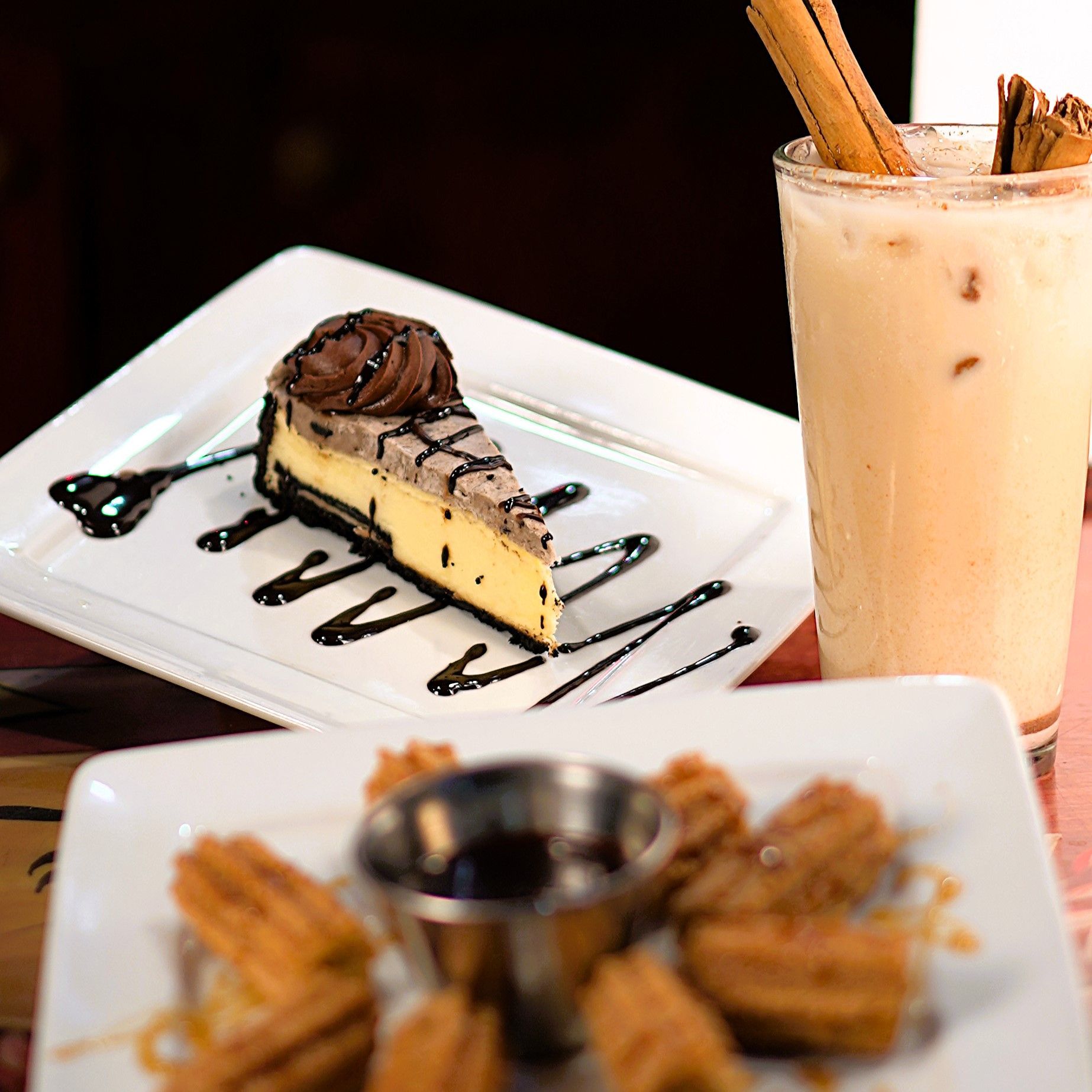 A plate of churros next to a plate of cheesecake and a milkshake