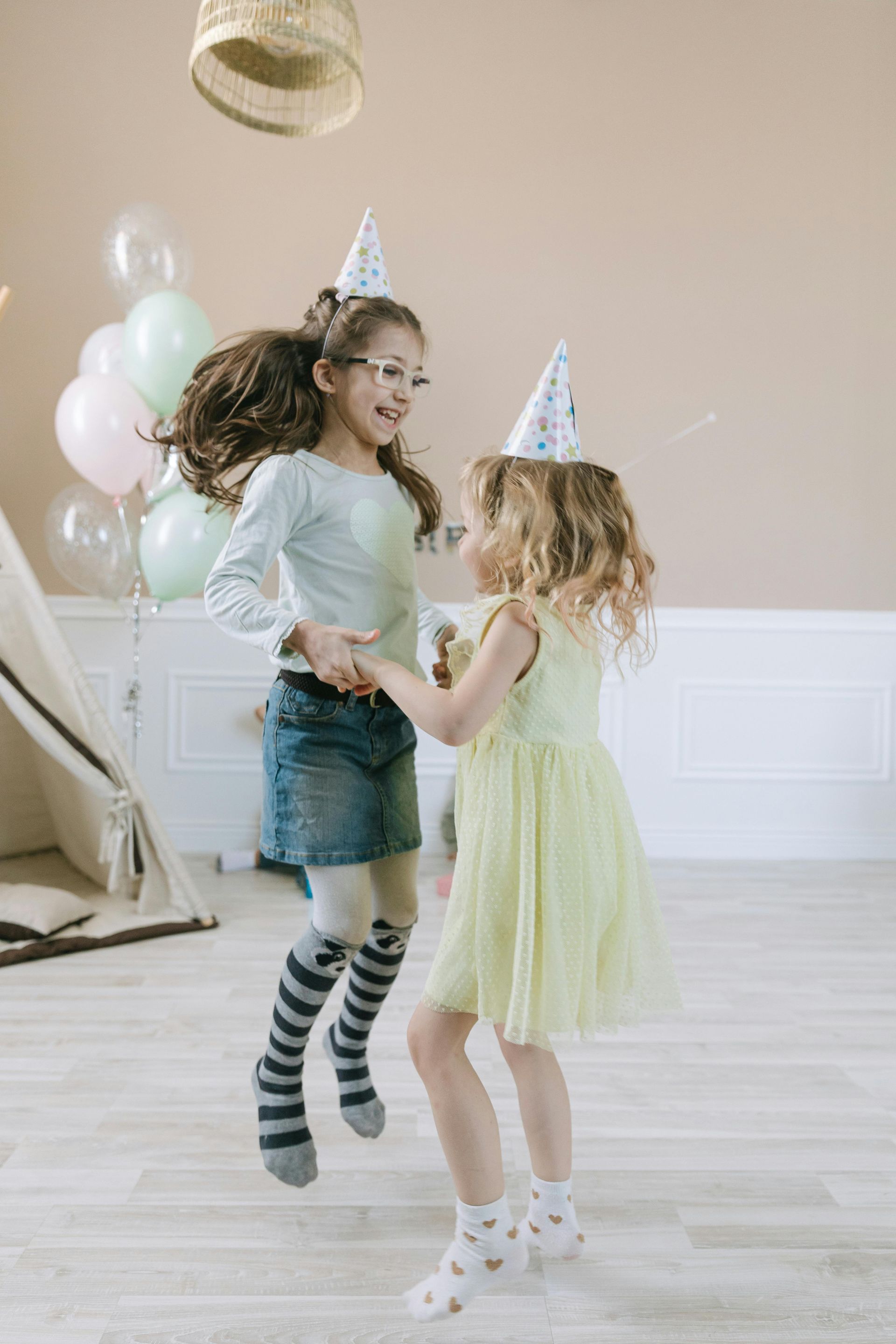 Two little girls are dancing together at a birthday party.