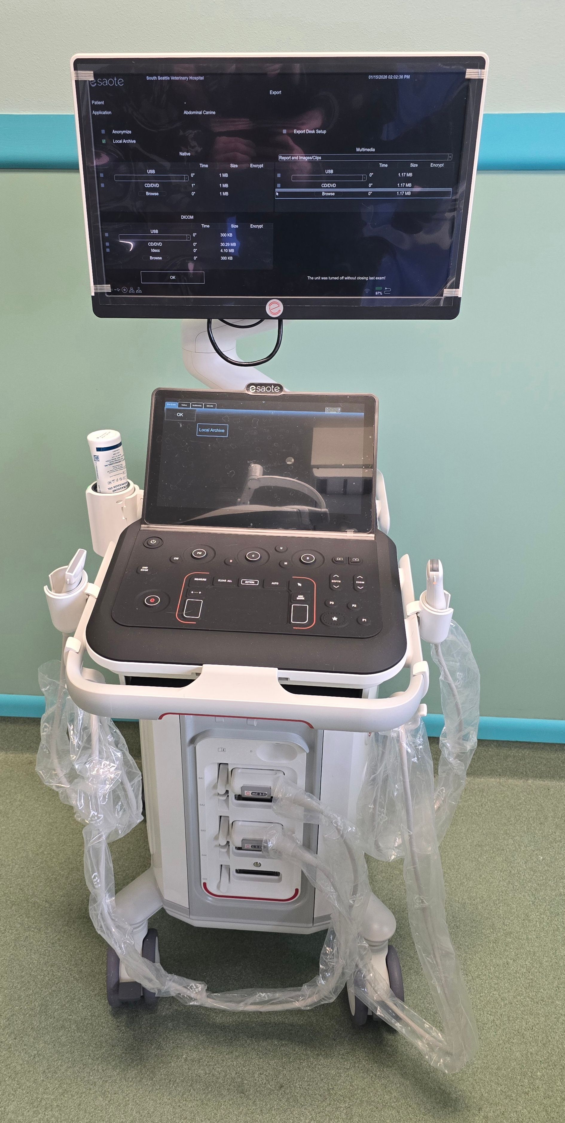 An ultrasound machine in a medical office. The machine has a monitor and keyboard, wrapped in plastic.