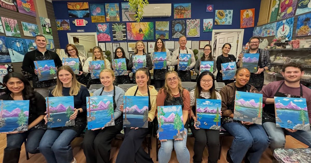 Group of people seated in a classroom holding colorful artwork in front of a wall of student art displays
