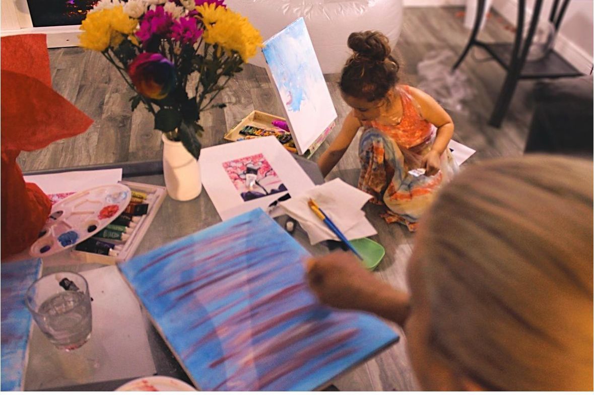 Two little girls are painting on a canvas on a table.