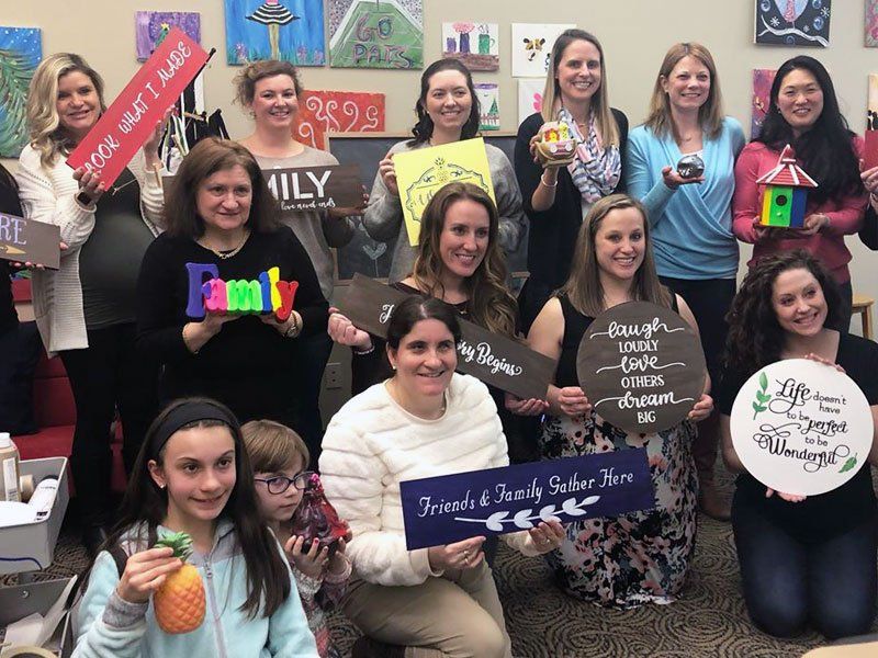 Group at paint and sip party posing with their paintings