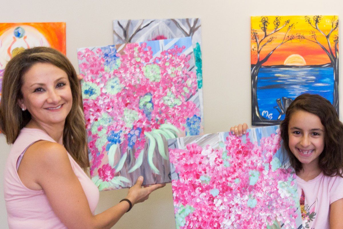 A woman and a girl are holding paintings in front of a wall.