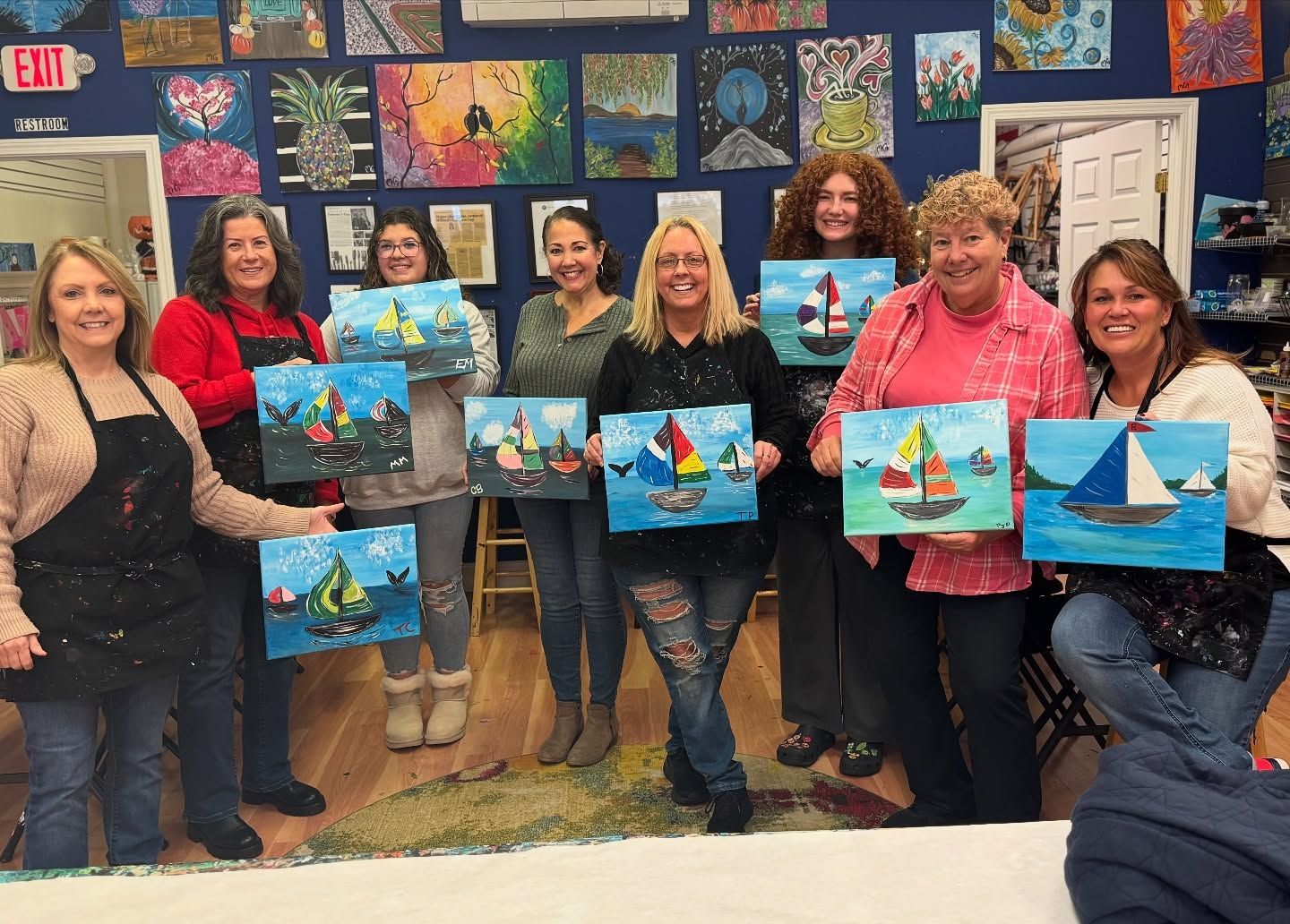 A group of women are holding paintings of sailboats in a room.