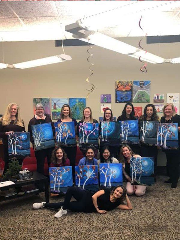 Group at paint and sip party posing with their paintings