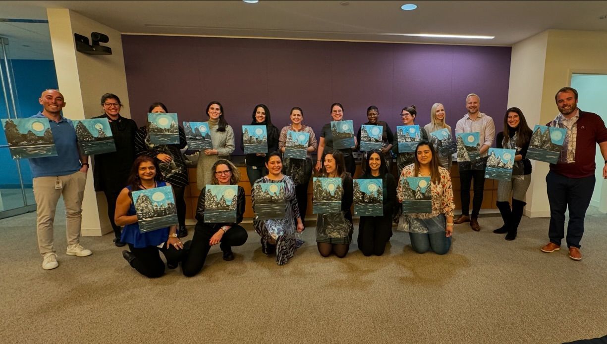 A group of people are posing for a picture while holding paintings.