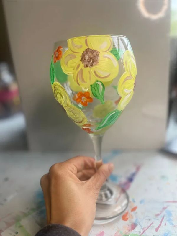 A person is holding a wine glass with flowers painted on it.
