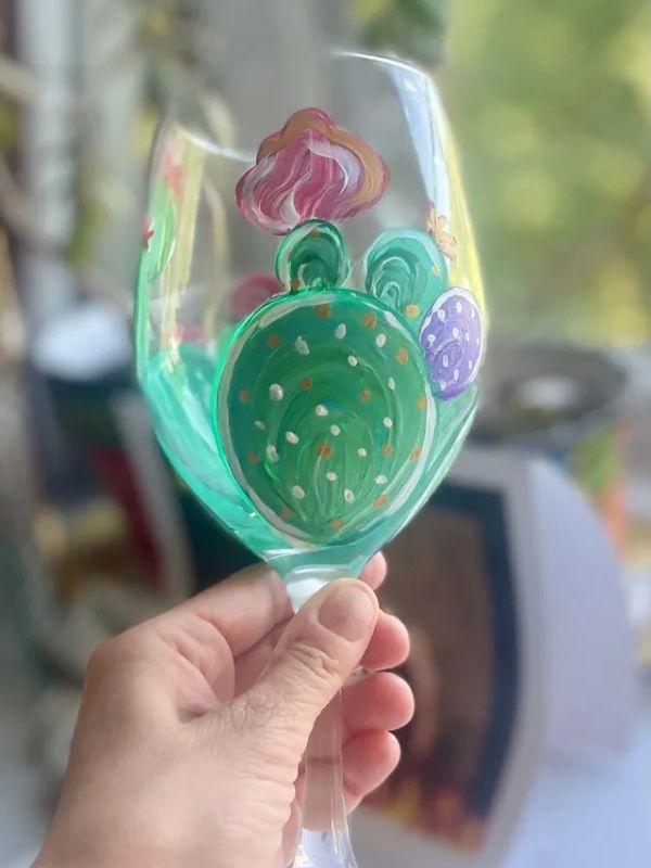 A person is holding a wine glass with a cactus painted on it.