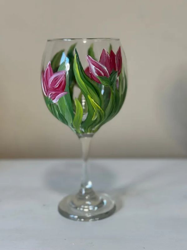 A wine glass with pink and green flowers painted on it