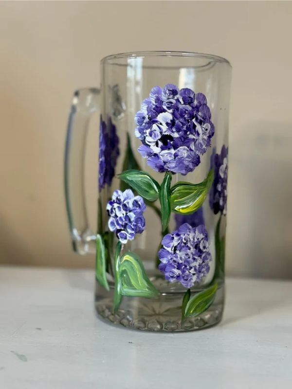 A glass mug with purple flowers painted on it