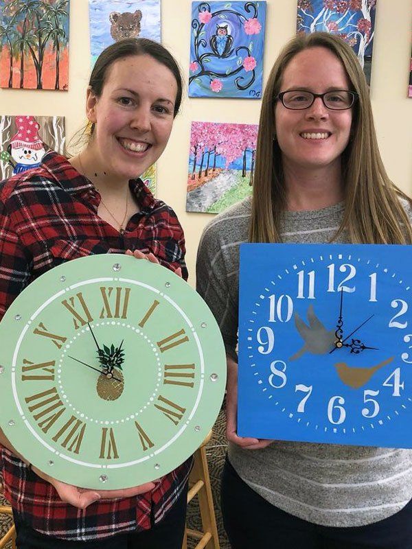 Two women posing with painted clocks
