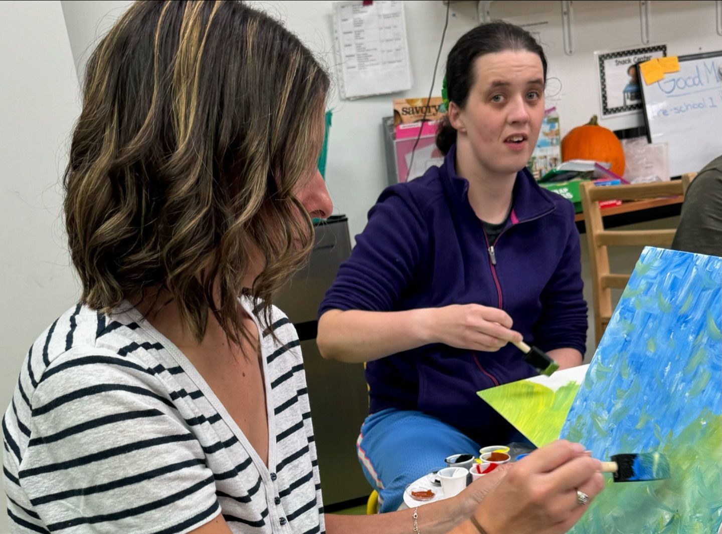 Two women are sitting at a table looking at a painting.