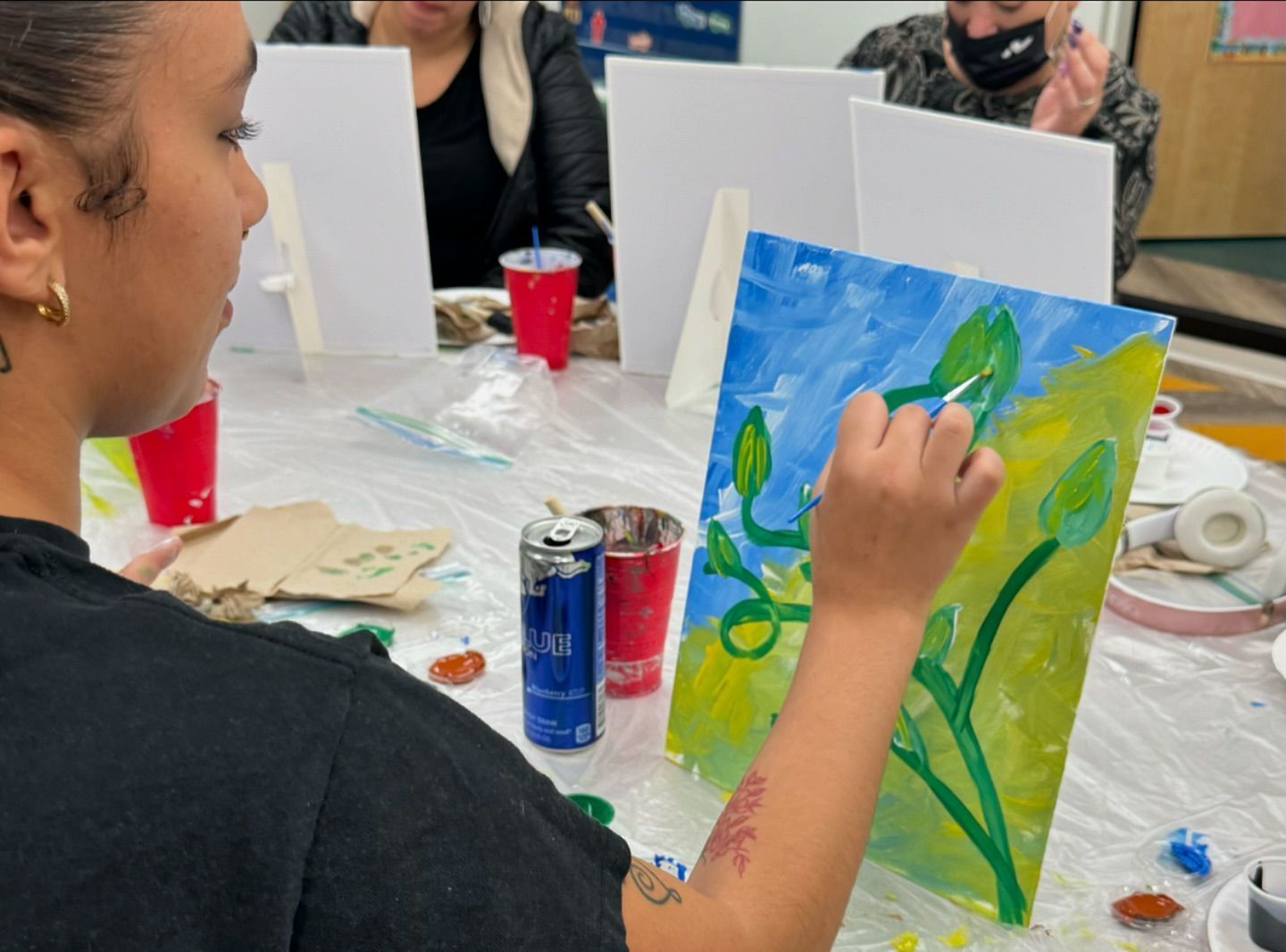 A woman is painting a picture of a plant on a canvas.
