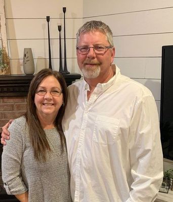 Owners Julie and Dave are posing for a picture in front of a fireplace