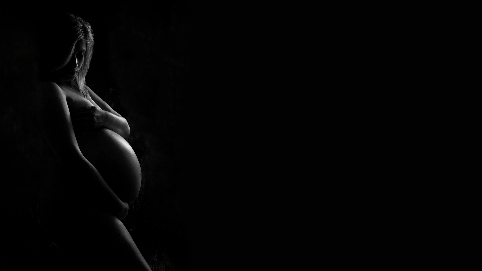 Een mooi met schaduwen belichte zwartwit foto van een zwangere vrouw tijdens een fotoshoot