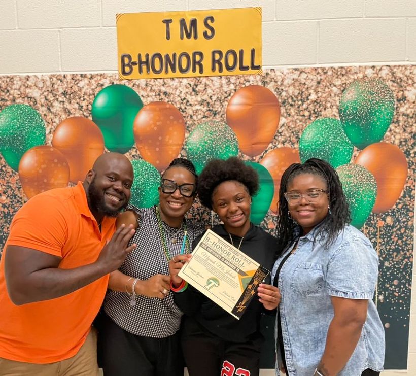 A group of people are posing for a picture in front of a sign that says tms b honor roll.