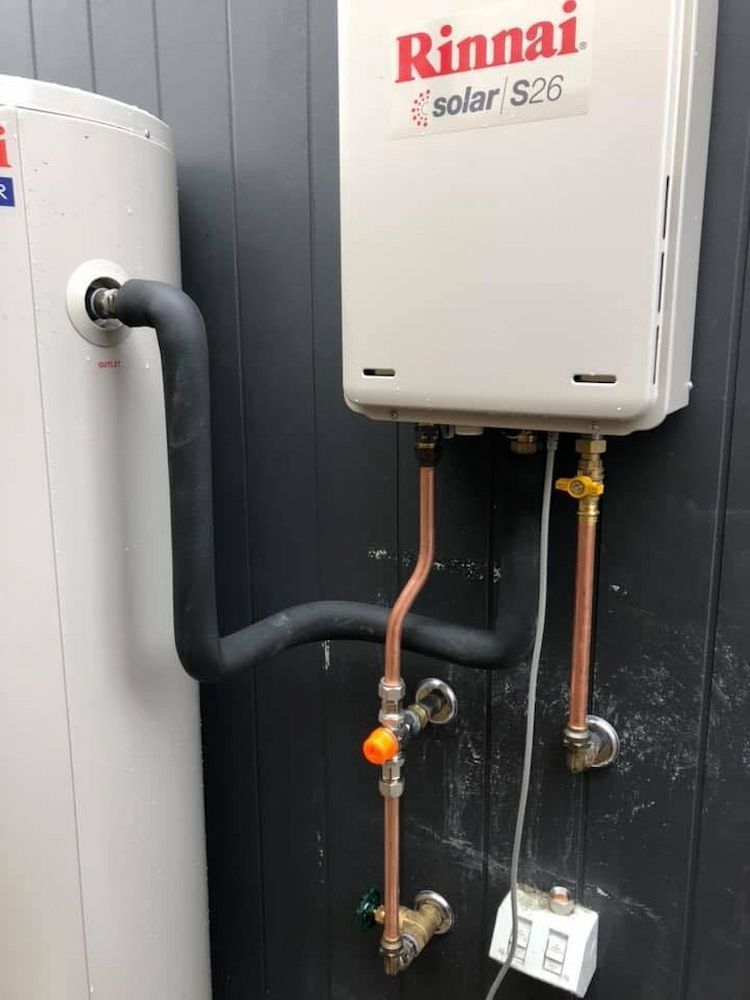 A Rinnai Water Heater is Attached to a Wall Next to a Water Tank — Peak Plumbing and Gas Fitting in Yamba, NSW