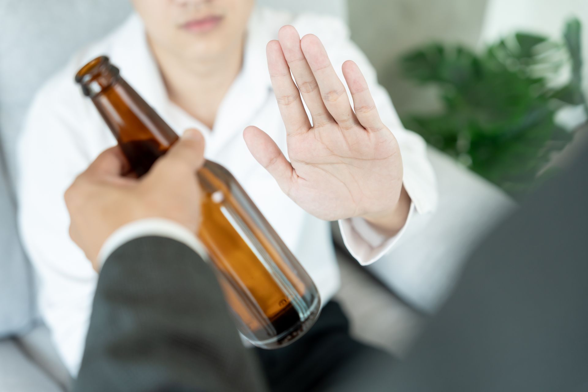Person raising a hand to refuse an offered bottle while another hand holds a brown glass bottle.