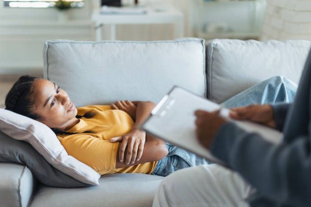 A woman is laying on a couch talking to a doctor.
