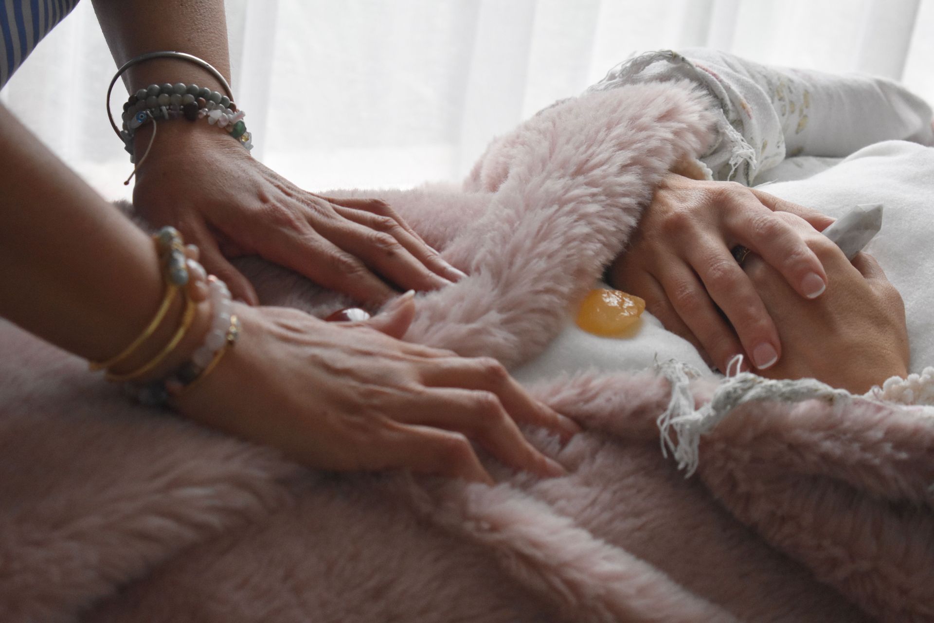 Hands on a person, receiving a treatment. Pink fluffy blanket. Light setting.