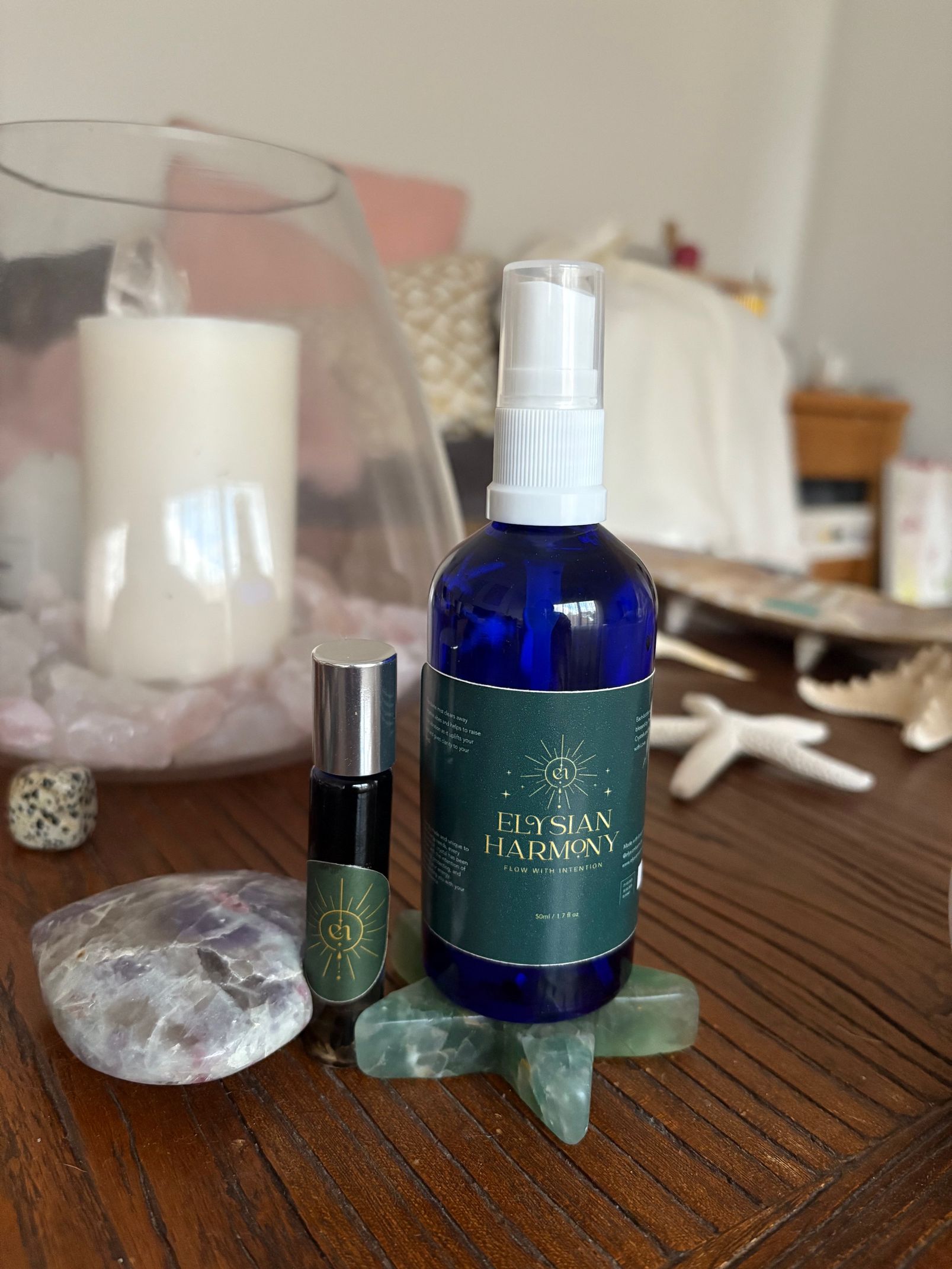 Two perfume bottles, one rollerball, and a spray bottle on a wooden table, next to a stone and candle.