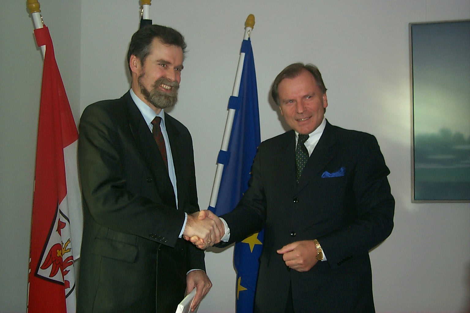 Zwei Männer in Anzügen schütteln vor Flaggen die Hände