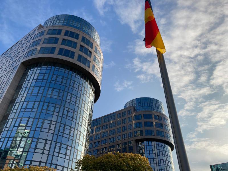 Vor einem hohen Gebäude weht eine deutsche Flagge.