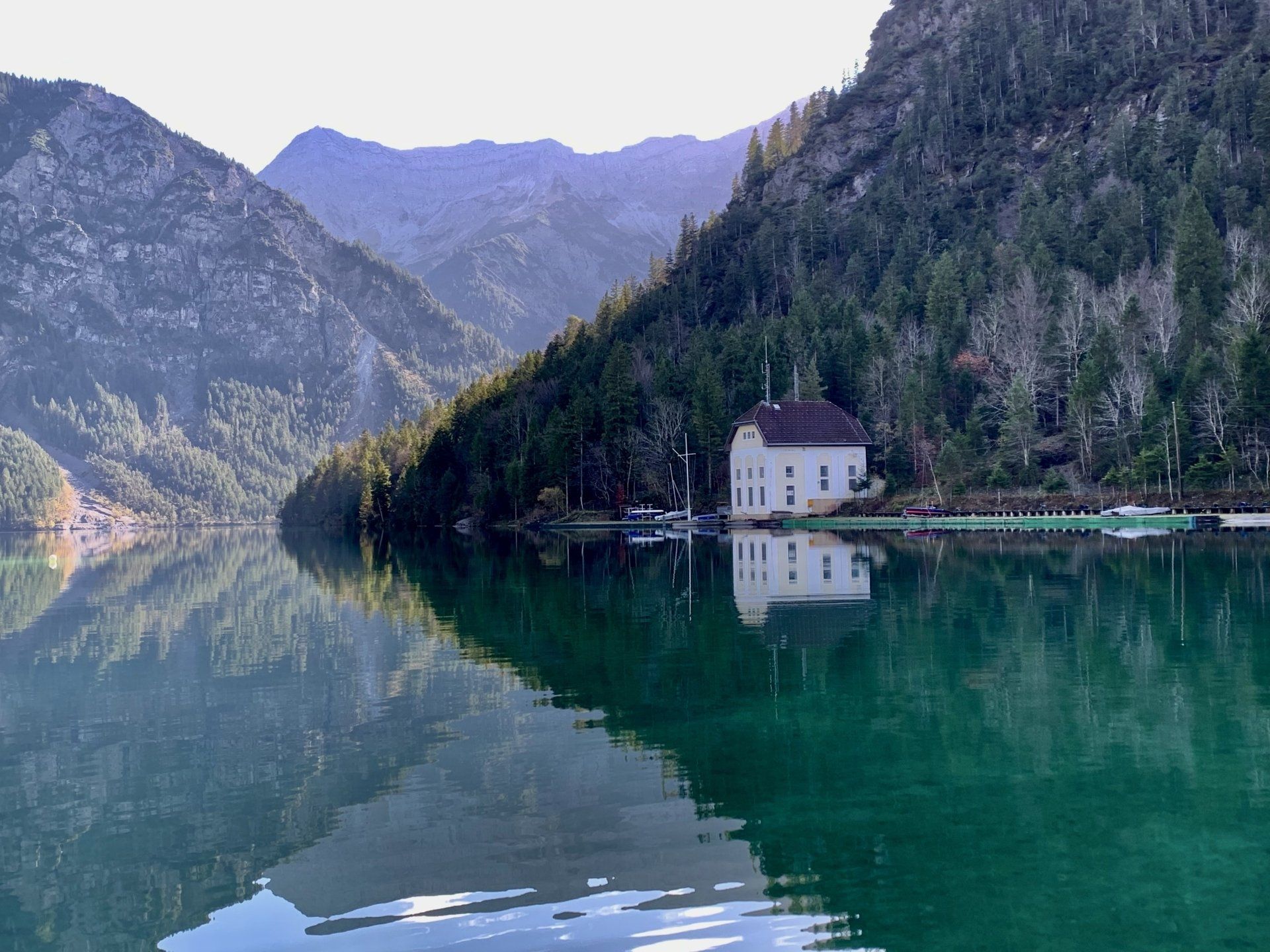 Ein kleines Haus liegt am Ufer eines Sees, umgeben von Bergen