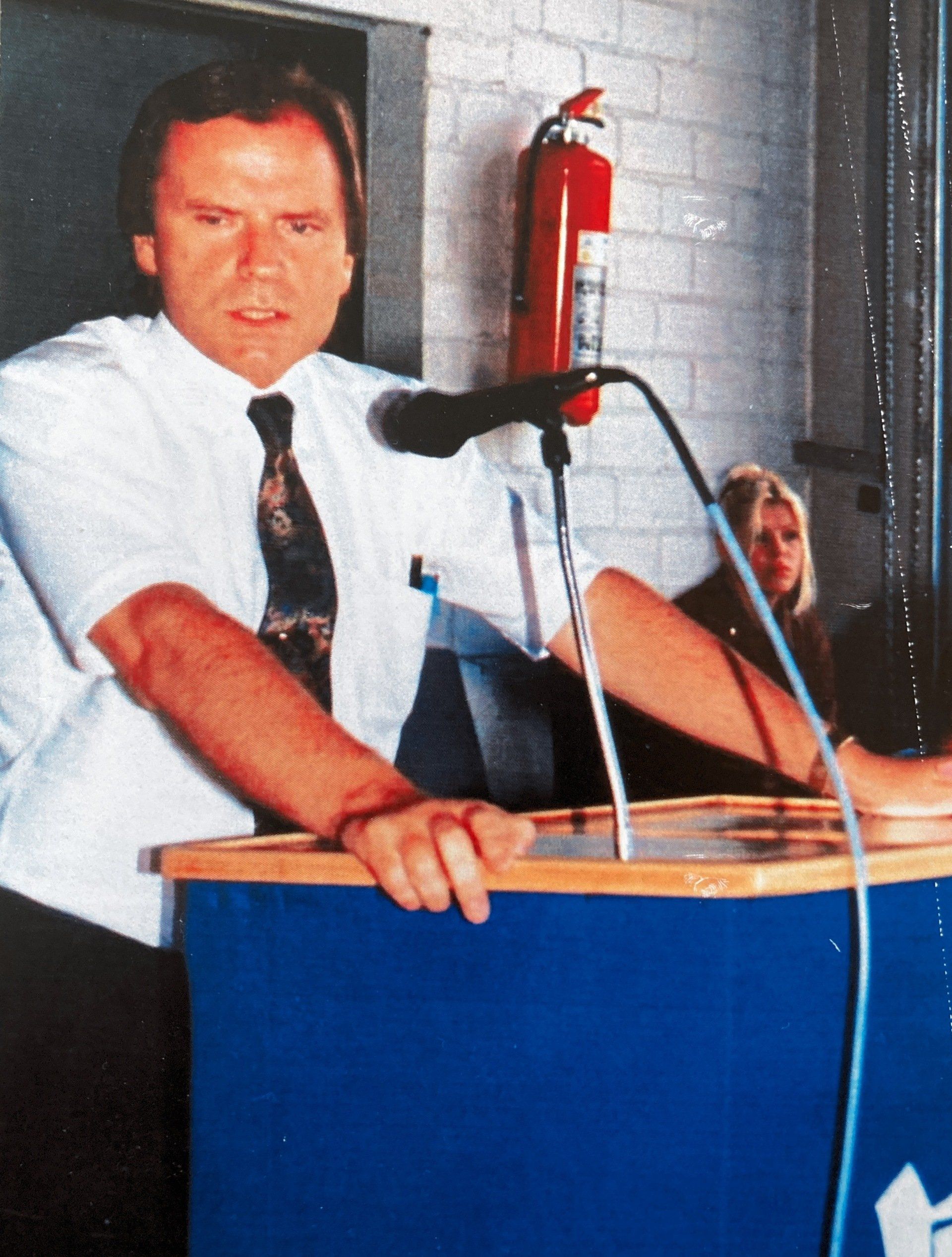 Ein Mann steht an einem Podium mit einem Feuerlöscher im Hintergrund