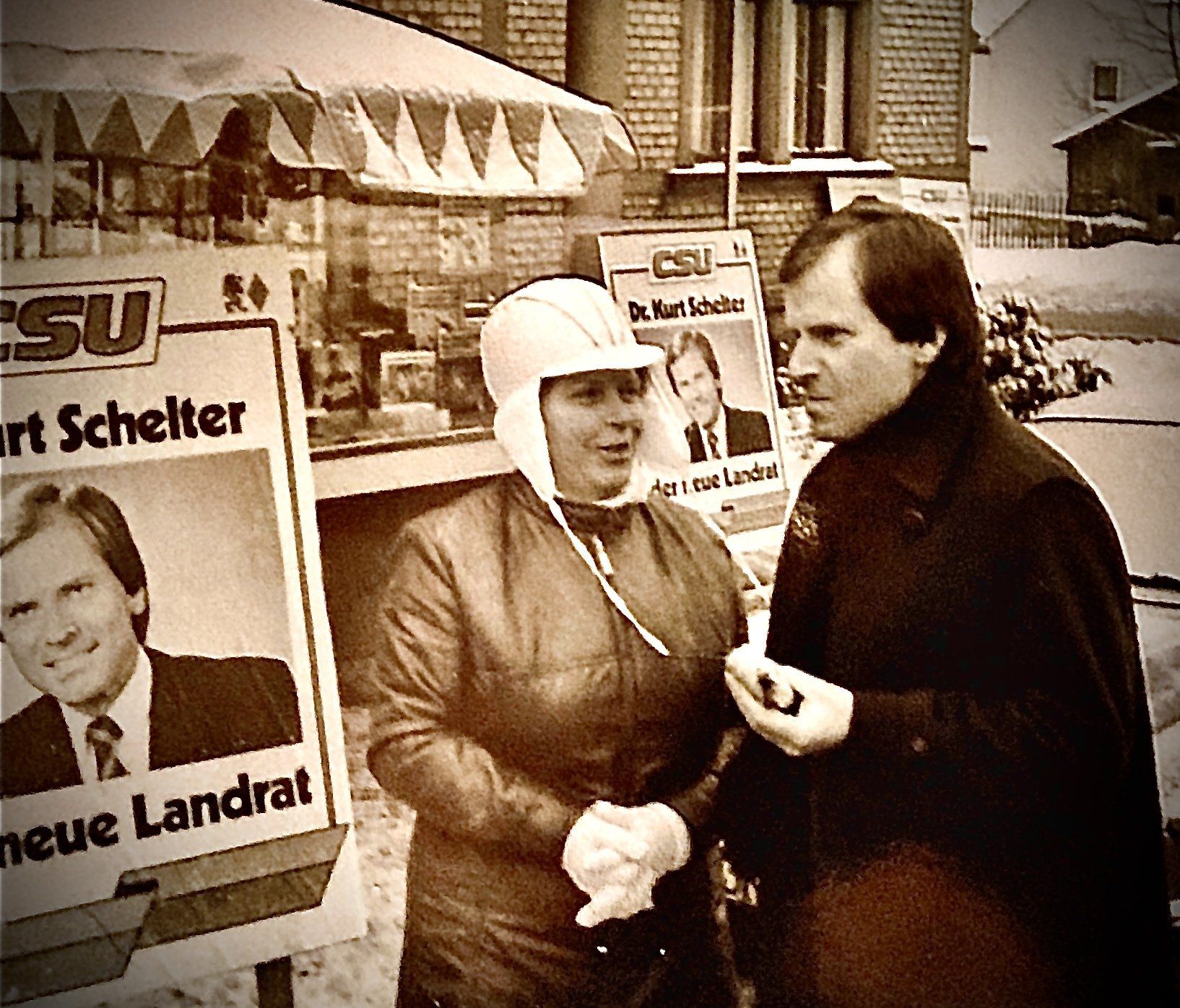 Ein Mann und eine Frau stehen vor einem Schild mit der Aufschrift „Neuer Landrat“